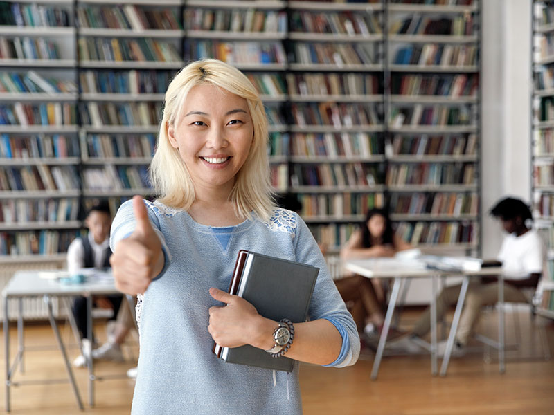 "Smiling trainee holding books doing a thumbs up, English for Asia "